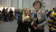 Die NDR-Reporterin Jasmin Al-Safi steht neben einer Angela Merkel Pappfigur.  