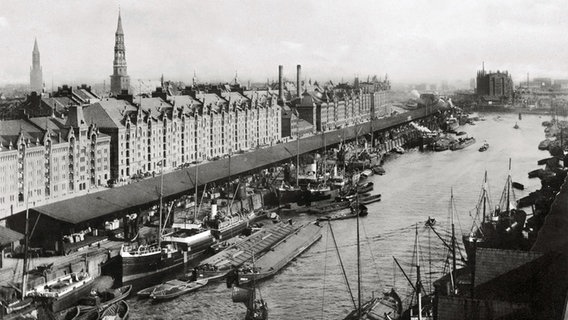 Sandtorhafen, etwa 1889: Seeschiffe liegen umringt von kleineren Schuten an der Kaimauer, dahinter die gerade errichtete Speicherstadt. Sandtorhafen, etwa 1889: Seeschiffe liegen umringt von kleineren Schuten an der Kaimauer, dahinter die gerade errichtete Speicherstadt. © Hamburger Hafen und Logistik AG