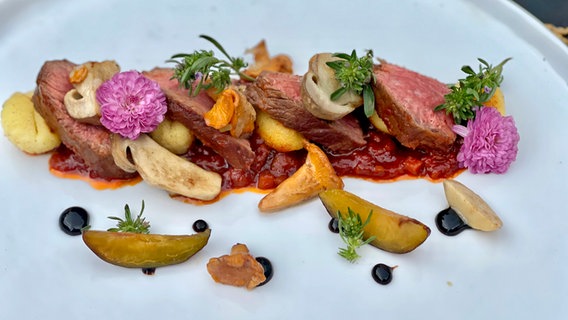 Lamm mit einer Pflaumen-Tomatensoße, gebratenen Pilzen und gebratenen Gnocchi ist auf einem Teller angerichtet. © NDR Foto: Dave Hänsel