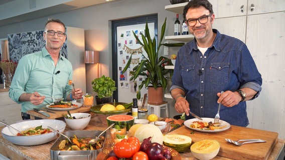 Fernsehkoch Tarik Rose (rechts) und Ernährungsmediziner Dr. Matthias Riedl stehen in einer Küche und essen Antipasti. © NDR Foto: Florian Kruck