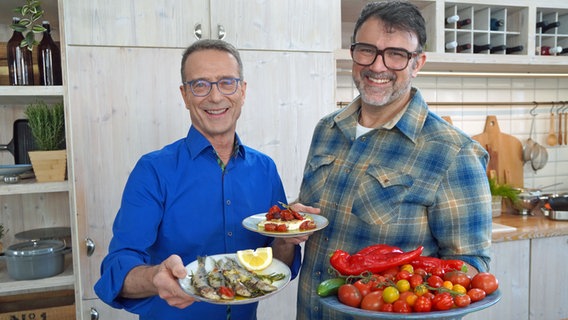 Tarik Rose und Ernährungs-Doc Matthias Riedl halten Teller mit Feta, Sardinen und Tomaten in die Kamera. © NDR Foto: Florian Kruck