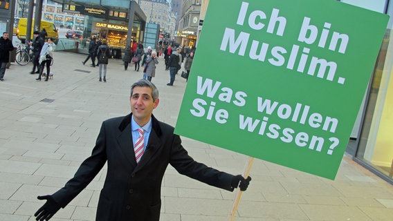 Michel Abdollahi hält ein grünes Schild hoch, auf dem steht: Ich bin Muslim. Was wollen Sie wissen? © NDR Foto: Stefan Mühlenhoff
