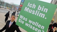 Michel Abdollahi hält ein grünes Schild hoch, auf dem steht: Ich bin Muslim. Was wollen Sie wissen? © NDR Foto: Stefan Mühlenhoff