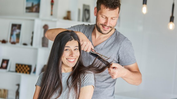 Ein Mann schneidet zu Hause einer Frau die Haarspitzen. © picture alliance/ Zoonar Foto: Robert Kneschke