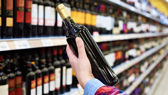 Rotweinflasche wird aus einem Regal im Supermarkt genommen © Fotolia.com Foto: Sergey Ryzhov