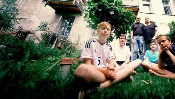 Vier Jungs sitzen im Schneidersitz im Gras. Hinter ihnen stehen Arm in Arm die Eltern. Dahinter ein Mietshaus. © WDR/Fritz Gnad 