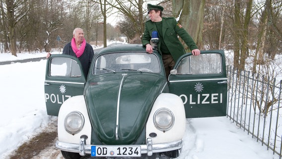 Szenenbild aus der 50. Büttenwarder-Folge "Fifty": Bürgermeister Schönbiehl steigt in den Polizeikäfer von Polizist Peter. © NDR/Nicolas Maack Foto: Nicolas Maack