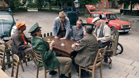 Szenenbild aus der 69. Büttenwarder-Folge "Topptach": Einige Dorfbewohner - Kuno, Dorfpolizist Peter, Adsche, Jürgen Seute, Bürgermeister Griem und Onkel Krischan sind vor dem Dorfkrug zusammengekommen. © Polyphon / Uwe Ernst für NDR 