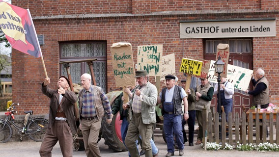 Szenenbild aus der 47. Büttenwarder-Folge "Freiheit": Die Büttenwarder demonstrieren vorm Dorfkrug. © NDR/Manju Sawhney Foto: Manju Sawhney