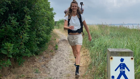 Eine junge Frau mit Rucksack wandert auf einem Küstenweg. © NDR 