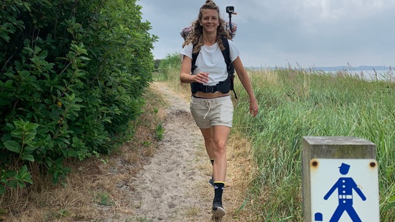 Eine junge Frau mit Rucksack wandert auf einem Küstenweg. © NDR 