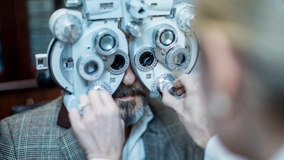 Ein Augenarzt lässt einen Patienten durch ein medizinisches Gerät blicken. © picture alliance / Westend61 Foto: zerocreatives