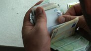 Ein Bündel Geldscheine in einer Hand ist zu sehen.  