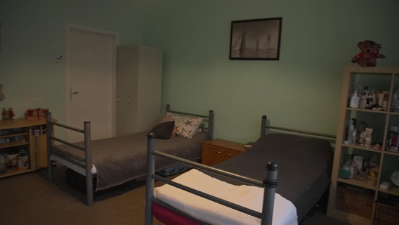 Ein Zimmer mit zwei Betten, zwei Regalen und einem Schrank. © NDR 