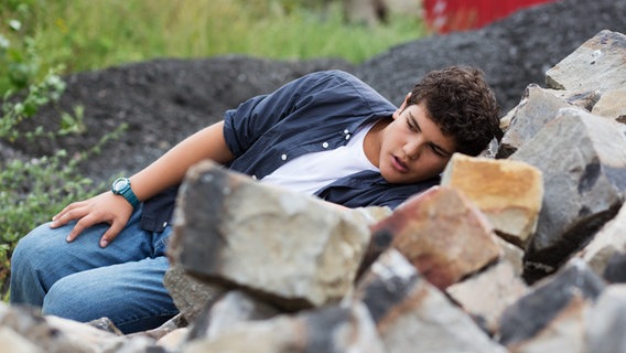 Anton (Danilo Kamber) liegt versteckt hinter einem Steinhaufen. © NDR Foto: Claudia Timmann
