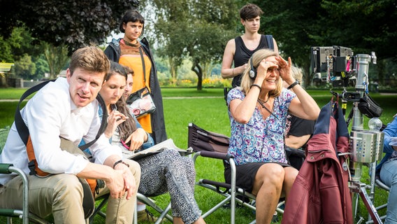 Mitglieder der Filmcrew sitzen auf Klappstühlen auf einer Rasenfläche. © NDR/Studio HH/Boris Laewen Foto: Boris Laewen