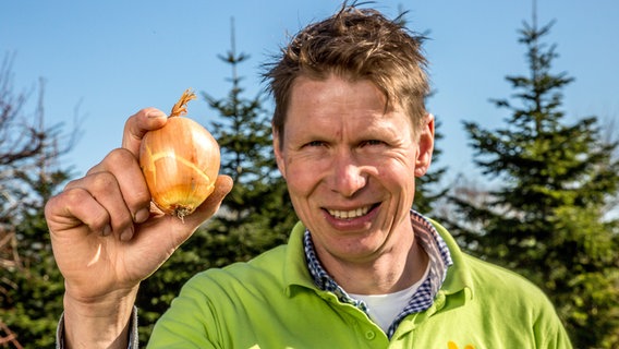 Gärtner Peter Rasch hält eine Zwiebel zwischen zwei Fingern. © NDR/Udo Tanske 