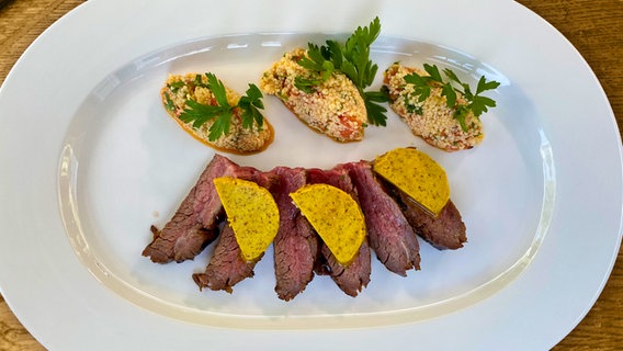 Flanksteak vom Grill mit Currybutter und Melonen-Taboulé auf einem Teller angerichtet. © NDR 