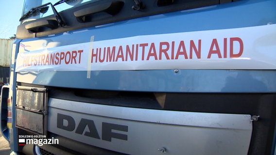 Ein Lkw träg vorne auf der Motorhaube eine Überschrift mit roten Buchstaben: "Hilfstransport Humanitarian Aid". © NDR 