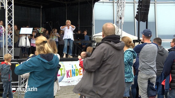 Erwachsene stehe vor einer Bühne an der Kieler Hörn und machen bei einer Animation mit Kindern auf der Bühne mit. © NDR 