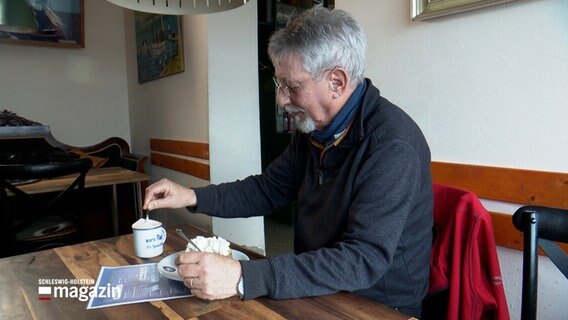 Ein Rentner sitzt in einem Cafe an einem Tisch mit einer Tasse Kaffee und einem Stück Kuchen. © NDR 
