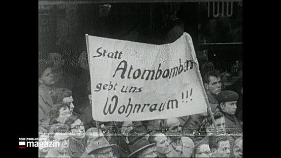 Eine historische Aufnahme zeigt Menschen bei einer Demo gegen eine deutsche Atombombe mit einem Banner, worauf steht: Statt Atombombe gebt uns Wohnraum!!! © NDR 