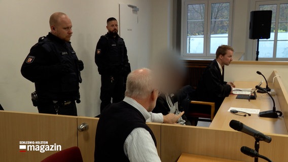 Ein Angeklagter sitzt neben seinem Verteiler und Polizisten in einem Gerichtssaal © NDR Screenshot Foto: NDR