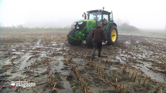 Ein Landwirt läuft über ein überschwemmtes Feld zu seinem Trecker © NDR Screenshot Foto: NDR