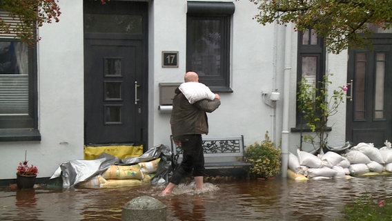 Eine Person trägt einen Sandsack durch Hochwasser. © NDR 