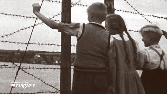 Eine historische Aufnahme zeigt Kinder, die an einem Stacheldrahtzaun im Flüchtlingslager Oksböl stehen. © NDR / Flugt Museum Oksbøl 