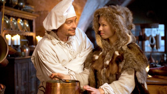 Allerleirauh (Henriette Confurius) und Matthis (Fritz Karl) stehen in einer Küche hinter einem Suppentopf und sehen sich an. © NDR/Marion von der Mehden 