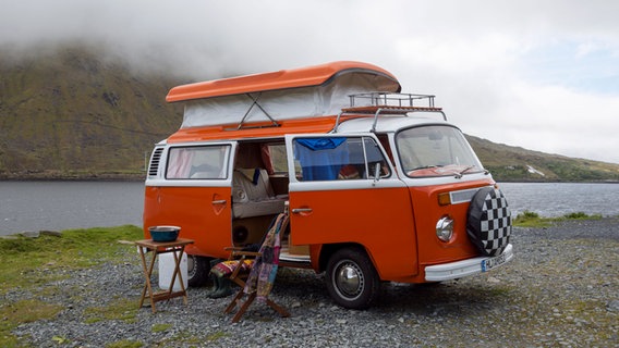 Ein alter VW-Bulli mit Campingausstattung steht an einem See. © picture alliance/imageBROKER Foto: Frauke Scholz