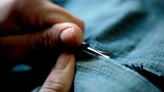 eine Jeans wird aufgetrennt, Screenshot aus der Dokumentation "Als die Jeans noch Nietenhose hieß".  