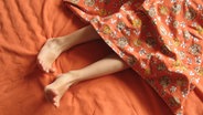 Beine einer Frau schauen unter einer Bettdecke hervor. © Colourbox Foto: Knud Nielsen