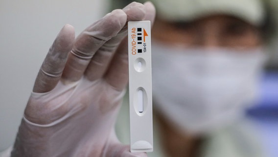 Eine Person in Schutzkleidung hält einen Antikörpertest in die Kamera. © picture alliance / AP/ dpa Foto: Lee Jin-Man