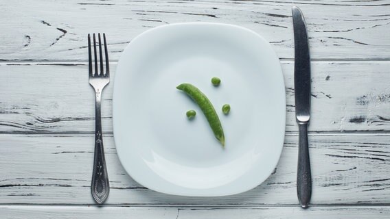 drei Ebsen und eine Ebsenschote liegen auf einem sonst leeren Teller mit Messer und Gabel. © fotolia Foto: alexmishchenko