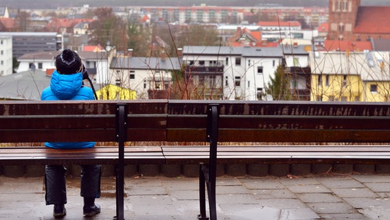 Eine junge Frau sitzt allein auf einer Bank und schaut auf eine Stadt. © Colourbox Foto: -