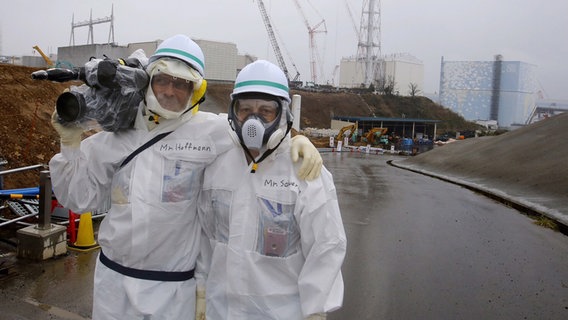 Korrespondent Uwe Schwering (re.) und Kameramann Bernd Hoffmann stehen in Schutzanzügen vor dem havarierten Atomkraftwerk in Fukushima Daiichi  