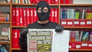 Ein "Titanic"-Redakteur mit Sturmhaube auf dem Gesicht hält eine Ausgabe der "Bild"-Zeitung hoch. © NDR 