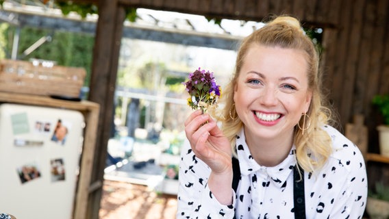 Köchin Zora Klipp hält ein Sträußchen frische Kräuter und Wiesenblumen in der Hand. © NDR Foto: Claudia Timmann