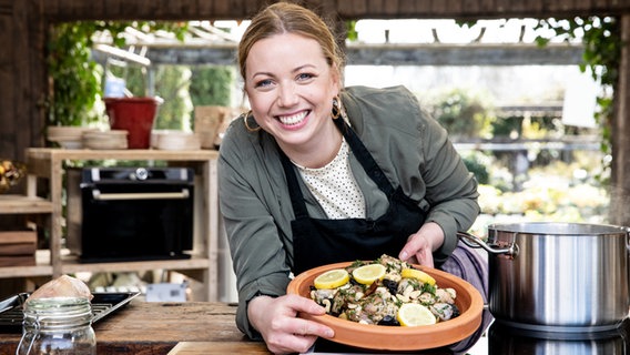 Köchin Zora Klipp steht am Tresen ihrer Outdoorküche und hält eine Tajine in der Hand. © NDR Foto: Claudia Timmann