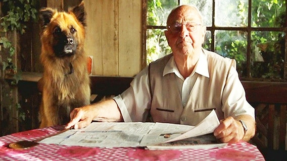 Ein Mann sitzt mit seinem Hund an einem Tisch  