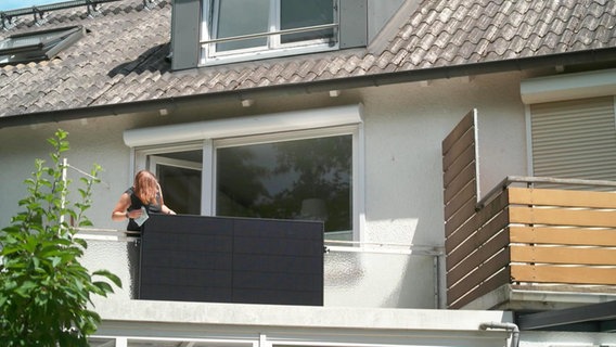 Eine Frau reinigt ein Solar-Panel an einem Balkon. © NDR 