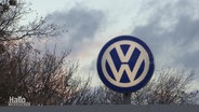 Zu sehen ist das VW-Symbol vor einem wolkenbehangenen Himmel.  