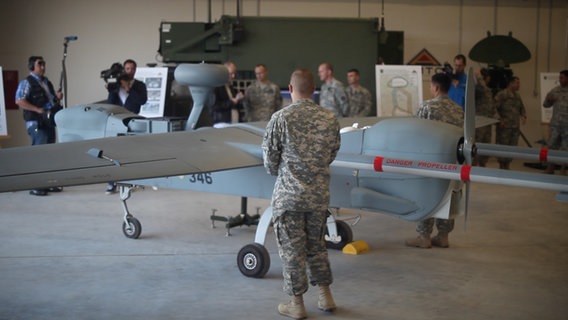 Ein Soldat in Uniform steht vor einer Drohne. Im Hintergrund filmt ein Kamera-Team. © NDR 