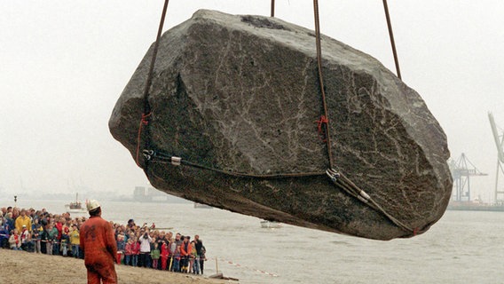 Ein riesiger Findling wird am 23. Oktober 1999 aus der Elbe an den Strand in Hamburg-Övelgönne gehoben, wo Zuschauer das Spektakel beobachten. © picture alliance Foto: Oliver Soulas