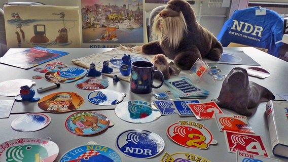 Aufkleber, Schlüsselanhänger und Figuren  mit der NDR Antje liegen auf einem Tisch © NDR Foto: Irene Altenmüller
