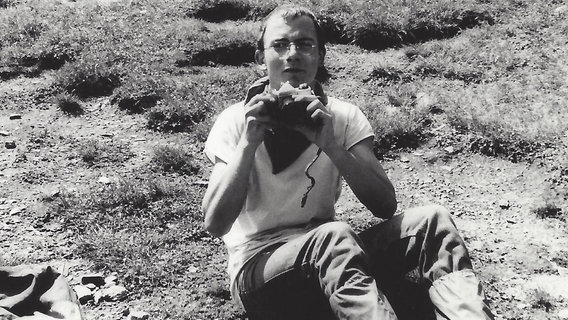Schwaz-weiß-Foto: Ein Mann sitzt auf einer Wiese, einen Fotoapparat in der Hand.  