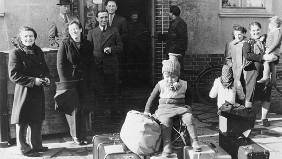 Bewohnende des jüdischen DP Camp Bergen-Belsen stehen im Jahr 1947 reisefertig mit Koffern vor einem Gebäude. © Public Domain Foto: Ursula Litzmann