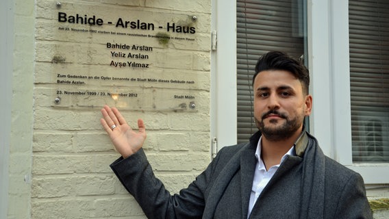 Ibrahim Arslan zeigt auf ein Schild an einem Haus mit der Aufschrift "Bahide-Arslan-Haus". © NDR Foto: Katrin Bohlmann